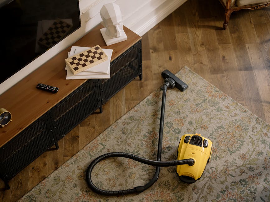 A professional cleaner from Biggin Hill Carpet Cleaners is performing deep surface cleaning in a bright, modern living room. The cleaner is dressed in a full white protective suit, gloves, a face mask